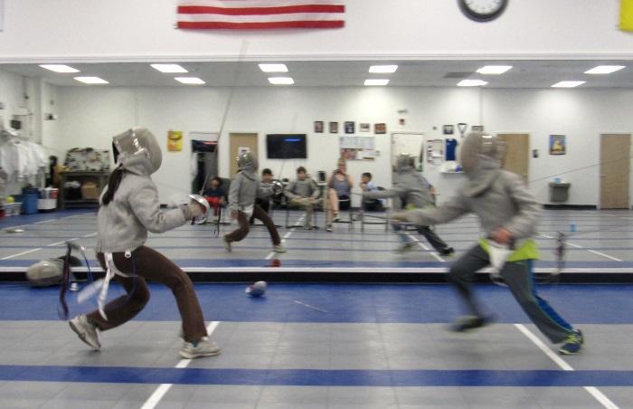 Campers in fencing gear practicing on indoor strips